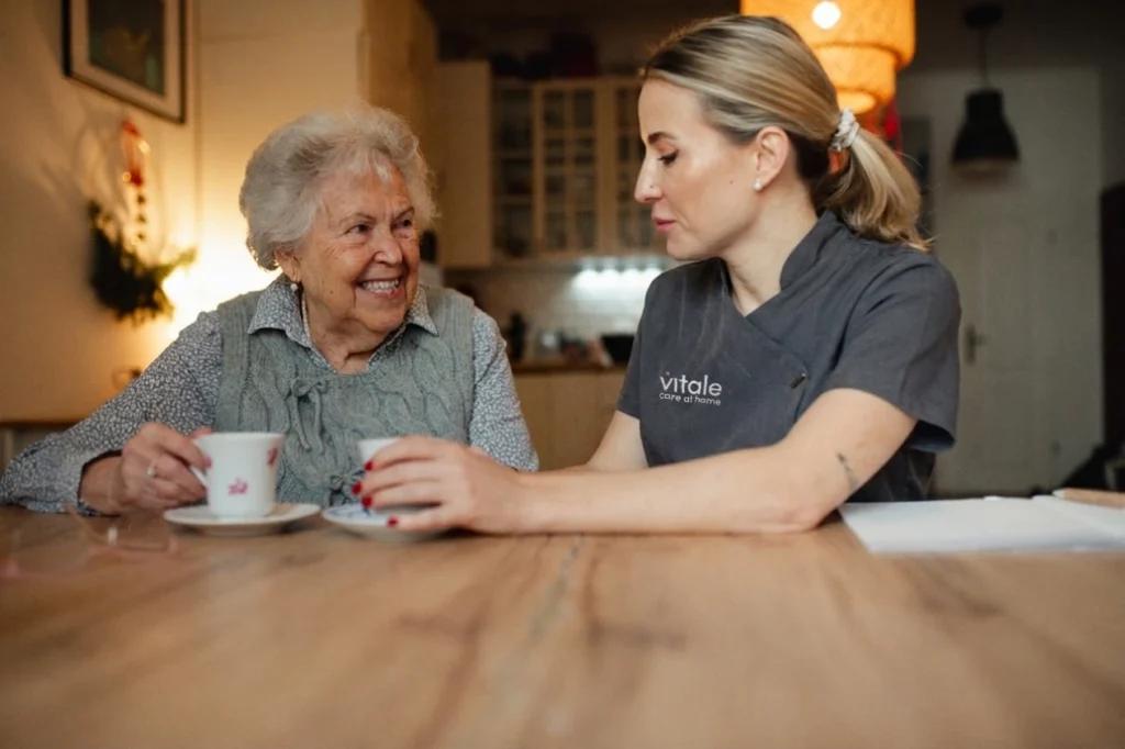 A Vitale Care live in care professional sitting at a table with an elderly lady enjoying a cup of tea.